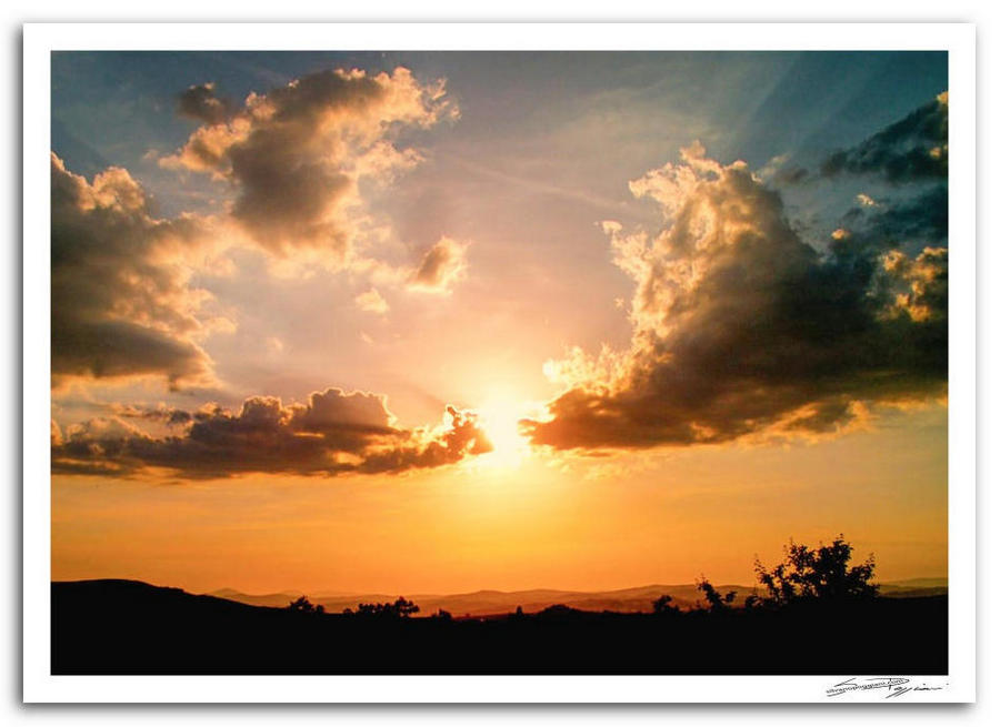 Tramonto arancione su paesaggio di campagna toscana con nuvole nel cielo.