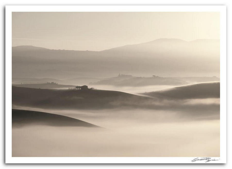 Paesaggio collinare toscano all'alba con nebbia che avvolge le valli, casolare in silhouette e morbide ondulazioni del terreno in controluce.